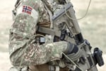 Bildet viser utsnitt av en soldat med det norske falgget på skulderen mens han holder et automatvåpen.
