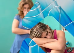 Ensom sammensunket jente med voksen som står bak og betrakter henne