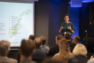 en kvinne i grønn bluse står på en talerstol foran en presentasjon
