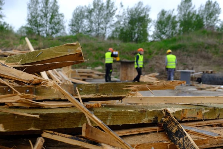 tre mennesker i gule refleksvester og hjelmer i bakgrunnen for revet treverk