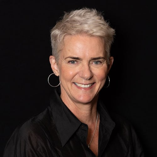 middelaldrende kvinne med kort lyst hår og store ringer i ørene, smiler