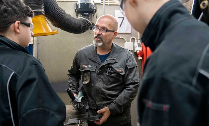 Lærer forklarer noe for videregående-elever på et verksted