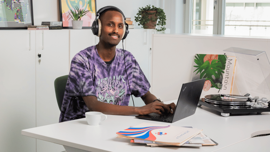 Ung melaninrik man sitter ved en PC og siler mot kamera